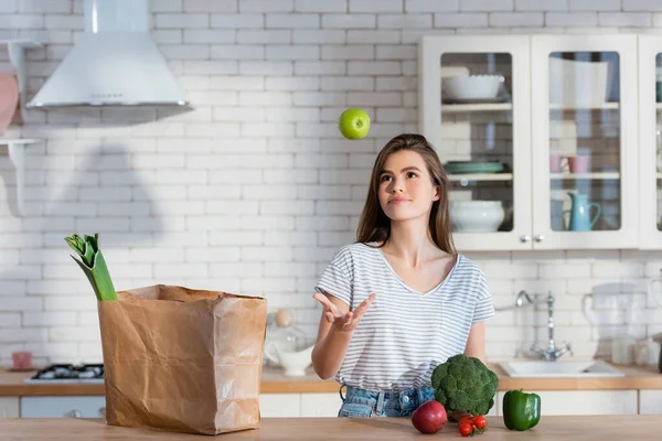 Smiling Woman Juggling Ripe Apple Paper Bag Fresh Vegetables Kitchen — Stock Photo, Image