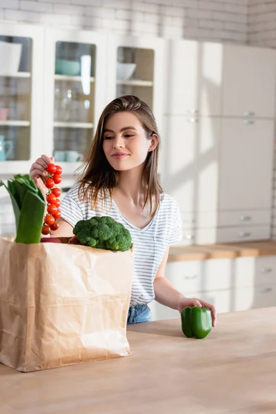 Glückliche Frau Hält Zweig Kirschtomaten Neben Papiertüte Mit Frischem Gemüse — Stockfoto