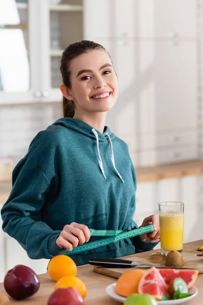 Mulher Feliz Olhando Para Câmera Medir Cintura Perto Frutas Frescas — Fotografia de Stock