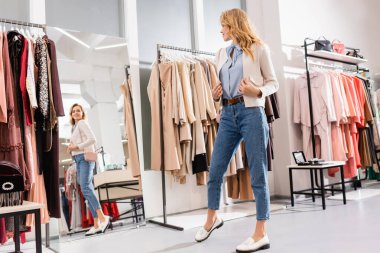 Ceketli, gülümseyen kadın galeride aynaya bakıyor. 