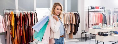 Güzel sarışın kadın, elinde alışveriş torbalarıyla kameraya gülümsüyor. 