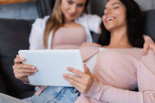 blurred and happy lesbian couple watching movie on digital tablet at home 