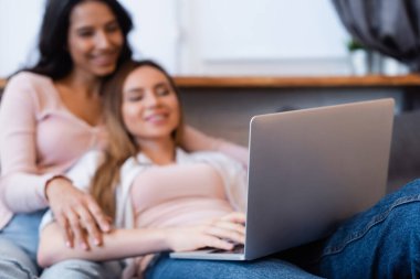 blurred and happy lesbian couple watching movie on laptop 