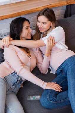 remote controller on couch near happy lesbian couple chilling at home