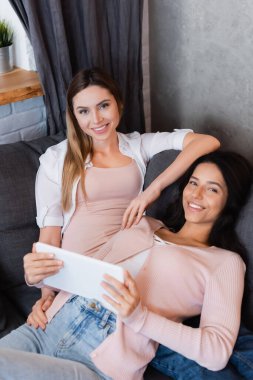 happy lesbian couple watching movie on digital tablet at home 