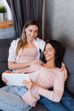 smiling lesbian couple watching movie on digital tablet at home 