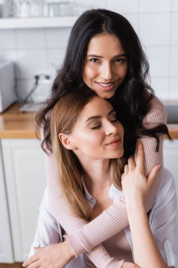 smiling lesbian couple embracing in kitchen 