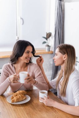 happy lesbian couple looking at each other near breakfast on kitchen table 