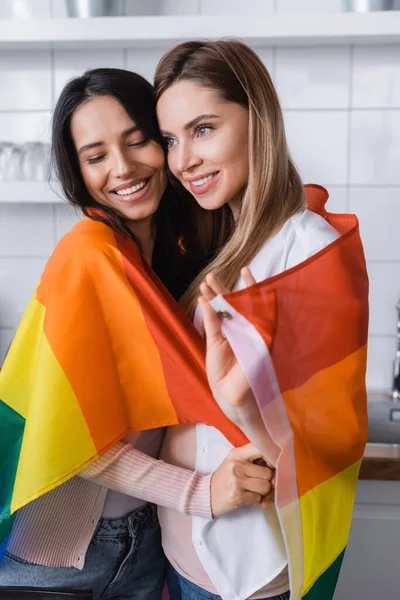 Cheerful Lesbian Couple Holding Lgbt Flag While Hugging Home — Stok fotoğraf