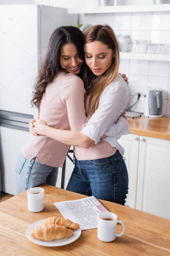 happy girlfriends hugging near breakfast on table  