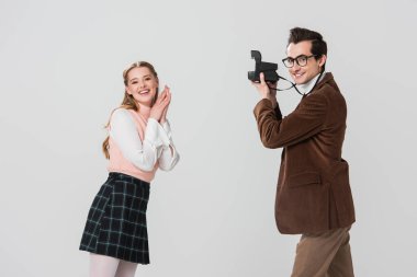 Gri renkte izole edilmiş eski moda fotoğraf makinesi olan adamın yanında poz veren eski moda elbiseli mutlu kadın.
