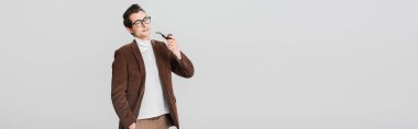 Gri pankartta izole edilmiş sigara piposuyla poz verirken kameraya bakan eski moda adam.