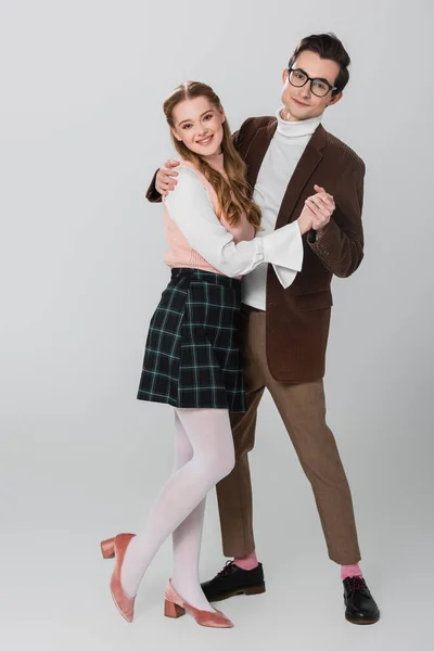 cheerful, old fashioned couple looking at camera while dancing on grey