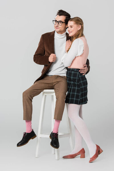 smiling woman in plaid skirt near retro style man sitting on high stool on grey background