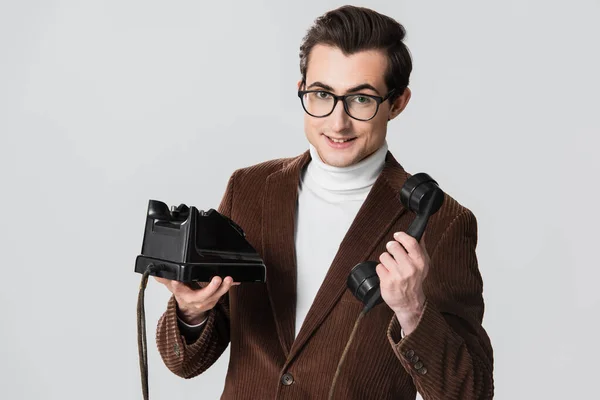 穿着棕色夹克的年轻人一边拿着用灰色隔离的老式电话一边对着相机微笑 — 图库照片