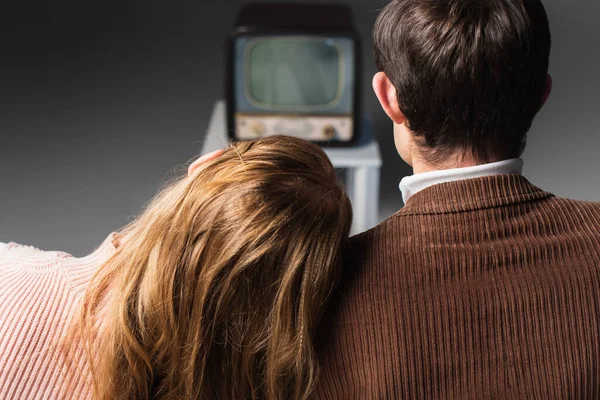 back view of woman leaning on shoulder of man while watching vintage tv on grey background