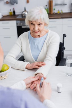 Hemşireye bakan yaşlı bir kadın bulanık arka planda insülin enjekte ediyor.