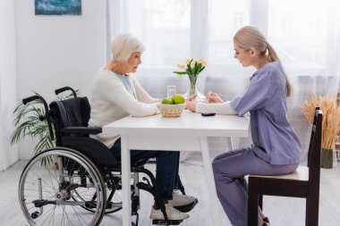 Tekerlekli sandalyedeki engelli yaşlı kadına insülin iğnesi yaparken yan görüş.