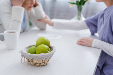 selective focus of fresh apples near nurse calming senior woman sick on dementia, cropped view clipart