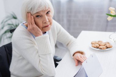 aged woman, sick on dementia, touching head while looking at camera near calendar clipart