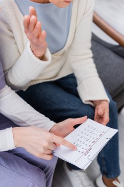 cropped view of social worker pointing at calendar near senior woman suffering from memory loss clipart