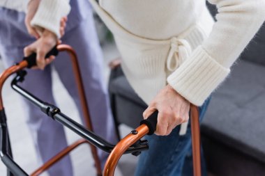 cropped view of social worker supporting aged woman walking with medical walkers clipart