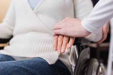 Tekerlekli sandalyedeki engelli kadının eline dokunan sosyal görevli görüntüsü.