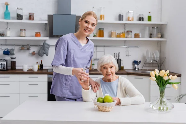 Young Nurse Senior Woman Smiling Camera While Holding Glass Water — Stock Photo, Image