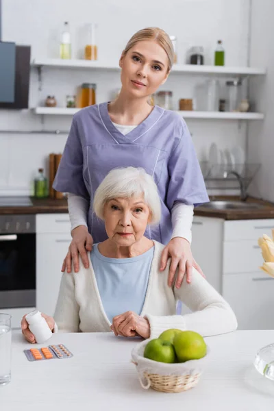 Young Nurse Looking Camera While Touching Shoulders Senior Woman Holding — Stock Photo, Image