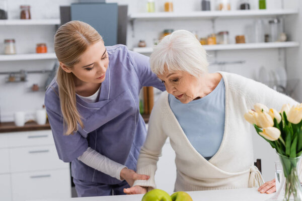 молодая медсестра помогает пожилой женщине встать на кухню