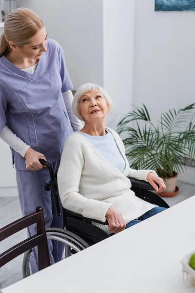 若い看護師は車椅子に座っている高齢障害者の女性を見て — ストック写真