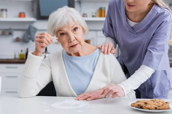 Ältere Frau Zeigt Puzzleteil Während Krankenschwester Ihre Schulter Berührt — Stockfoto