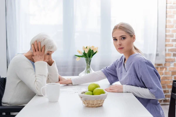 Young Nurse Looking Camera While Calming Upset Senior Woman Jigsaw — Stock Photo, Image