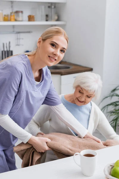 Junge Krankenschwester Lächelt Die Kamera Während Sie Seniorin Mit Weicher — Stockfoto