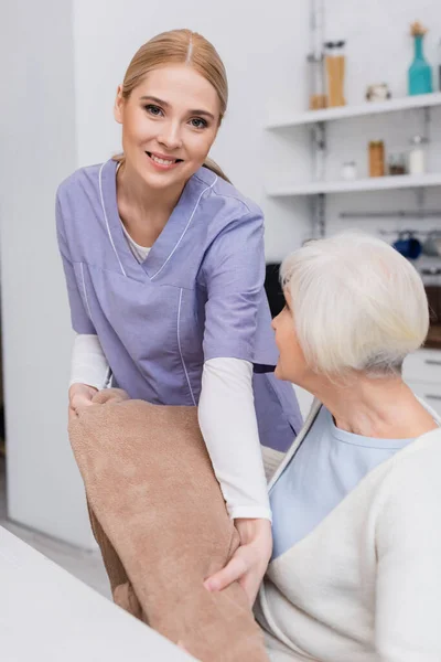 Felice Assistente Sociale Guardando Fotocamera Mentre Coperta Morbida Alla Donna — Foto Stock