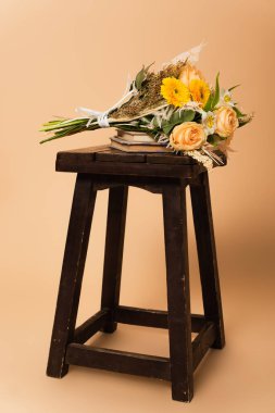 bouquet of different flowers on books and wooden chair on beige  clipart