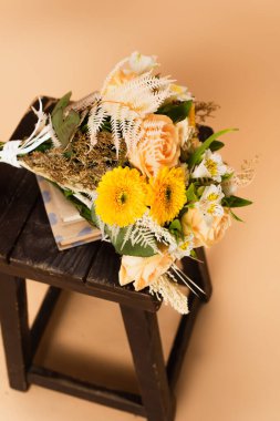 high angle view of bouquet with different flowers on books and wooden chair on beige  clipart