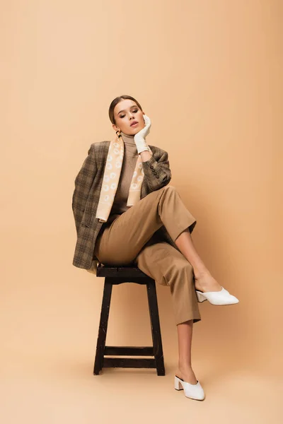 Fashionable Woman Blazer Pants Sitting Wooden Stool Beige Background — Stock Photo, Image