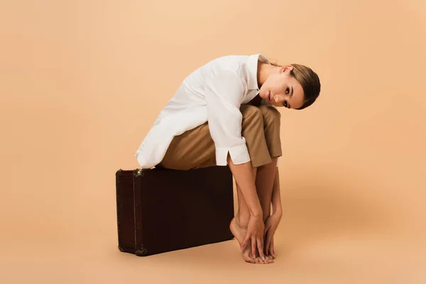 Barefoot Woman Shirt Trousers Touching Legs While Sitting Retro Suitcase — Stock Photo, Image