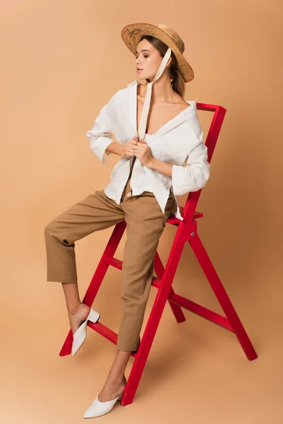 Vrouw Broek Wit Shirt Strohoed Zittend Rode Ladder Beige Achtergrond — Stockfoto