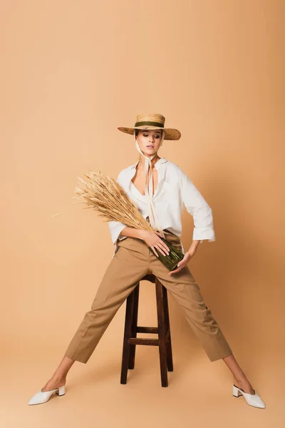 漂亮的女人 穿着时髦的衣服 头戴草帽 在米色的凳子旁边摆着尖刺 — 图库照片