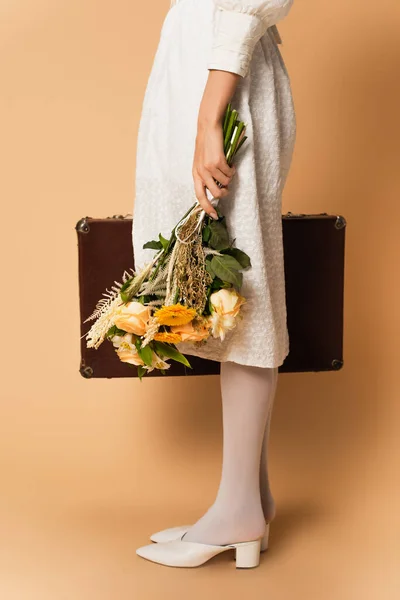 照片中穿着连衣裙的年轻女子拿着米色的花束和手提箱 — 图库照片
