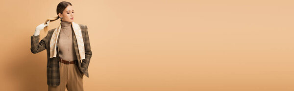 stylish woman in checkered blazer, pants and white gloves posing with hand in pocket on beige, banner