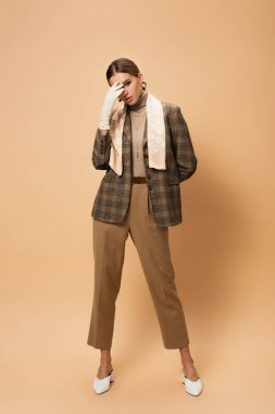 Kareli ceketli, pantolonlu ve bej renkli beyaz eldivenli şık bir kadın.