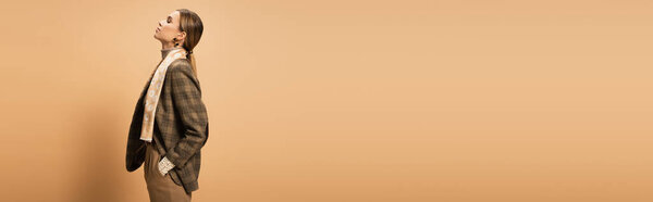 side view of stylish woman in checkered blazer posing with hand in pocket on beige, banner