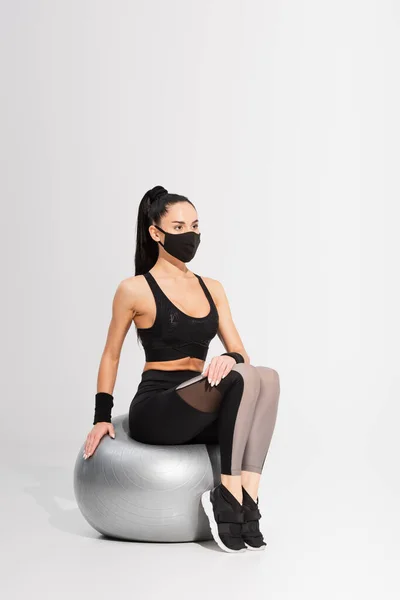 Junge Sportlerin Schwarzer Schutzmaske Sitzt Auf Fitnessball Auf Grau Stockbild