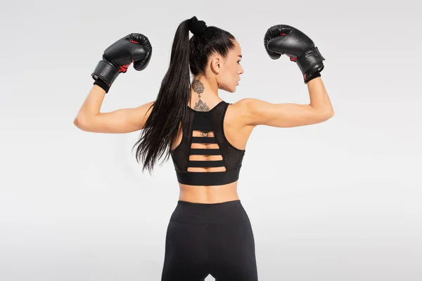 back view of tattooed sportswoman in boxing gloves isolated on grey