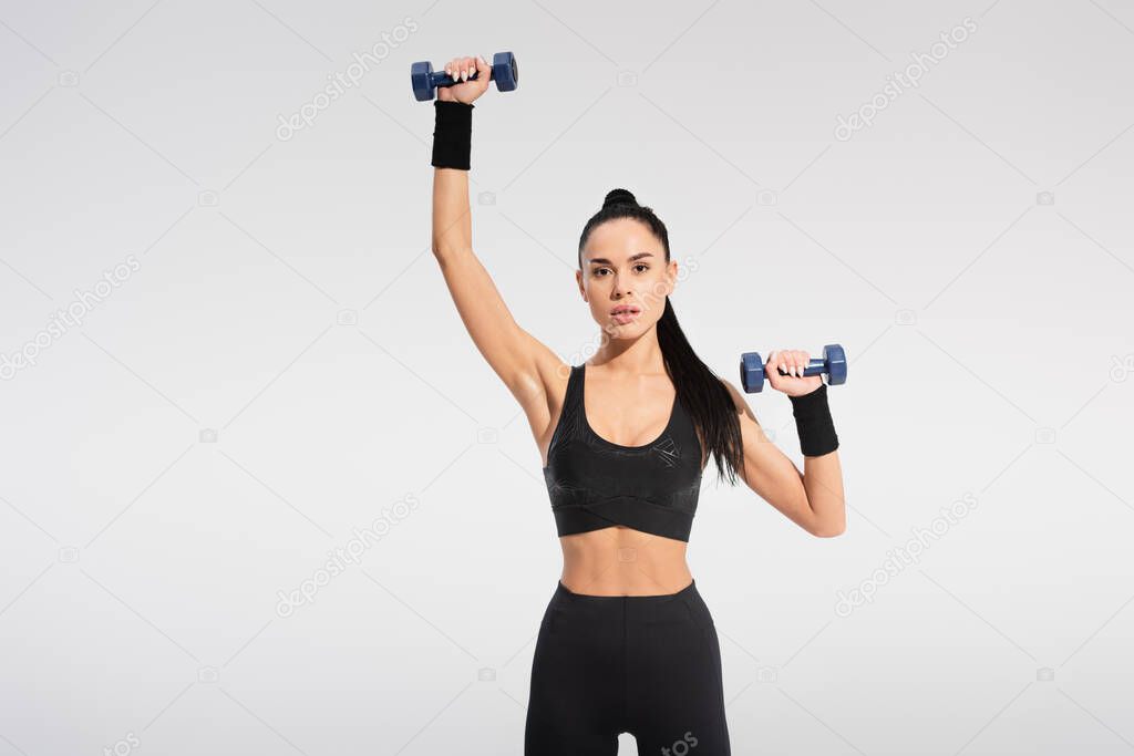 strong young sportswoman in sportswear exercising with dumbbells isolated on grey