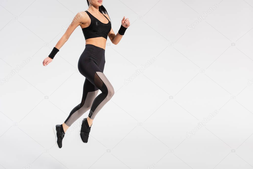 partial view of young woman in sportswear levitating on grey