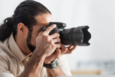 blurred latin man taking photo on modern digital camera in home studio clipart